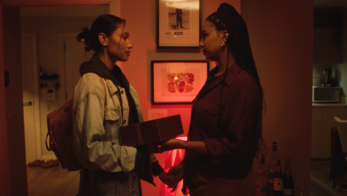 Still from Fish & Chips: two women facing each other in a warmly lit room, one holding a wrapped gift.
