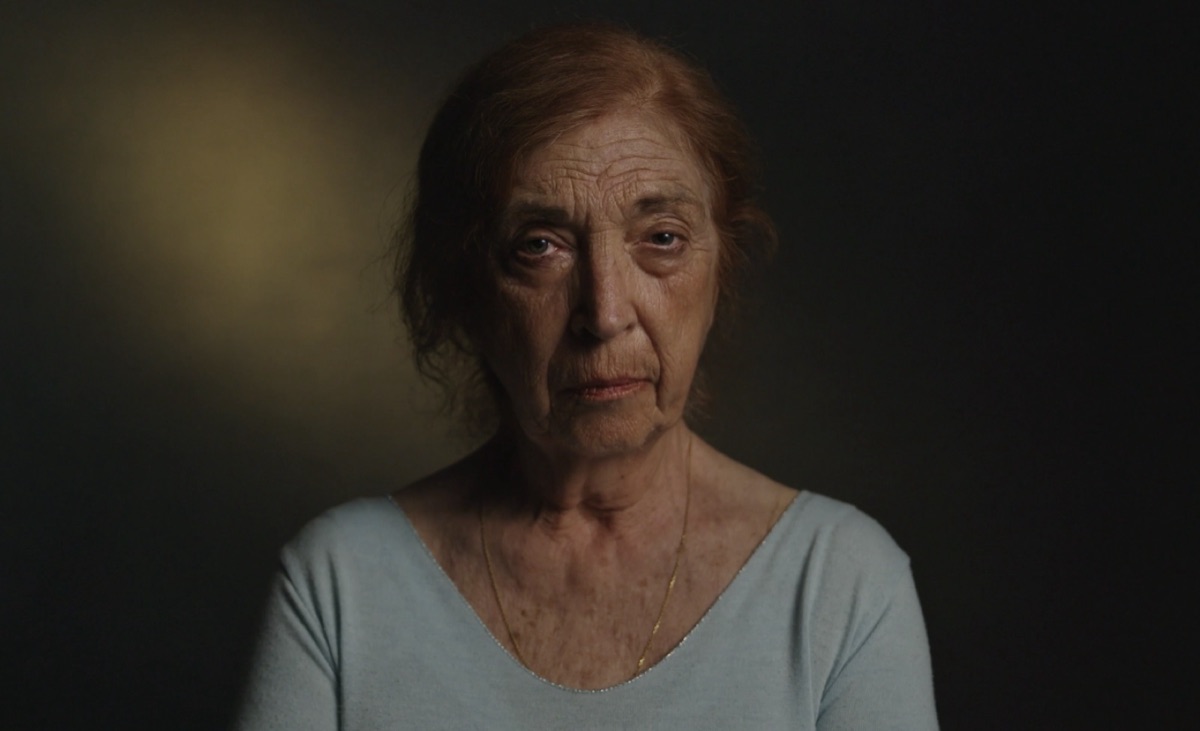 Still from 'It's Not Banter': an older woman looking into camera against a dark background.
