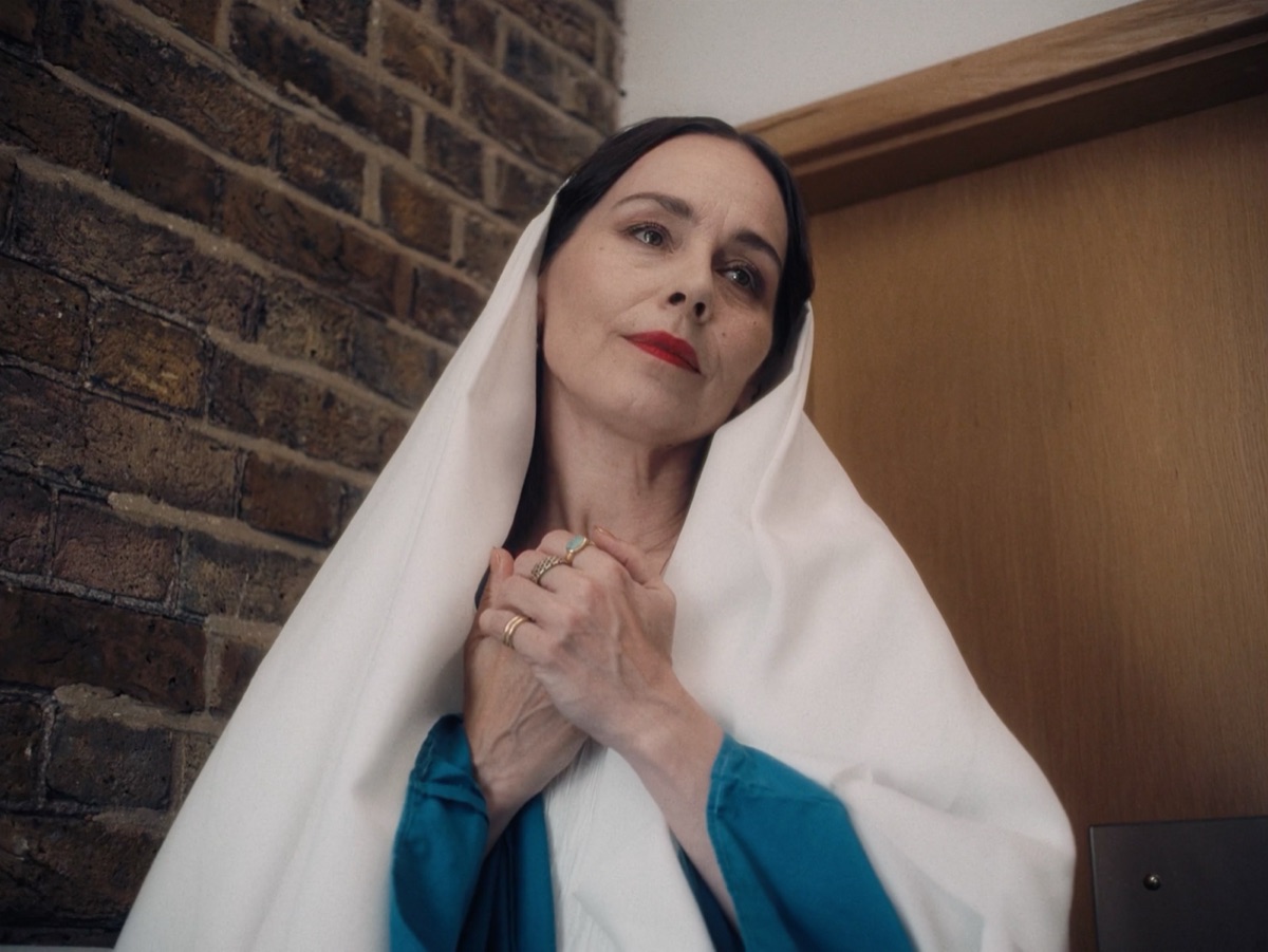 Still from Not a Mourning Person: a woman in a teal dress and white headscarf looking upward.