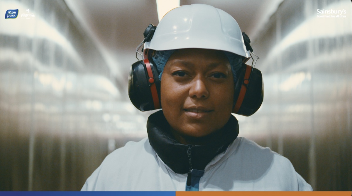 Still from the Sainsbury's partnership film: a factory worker in a hard hat and ear defenders facing the camera.