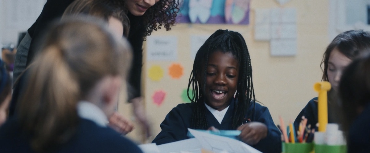 Still from Young Minds 'Welcome': a child smiling in a busy classroom.